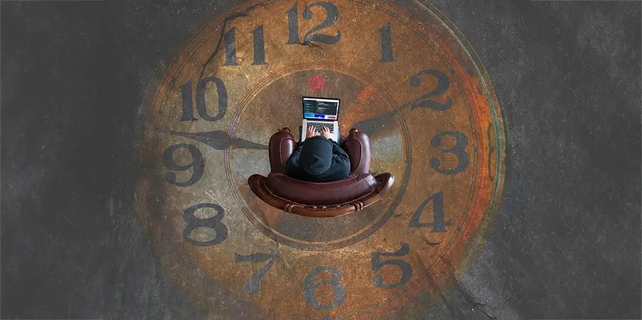 Persona sitting on a chair using a laptop in the middle of a large clock.
