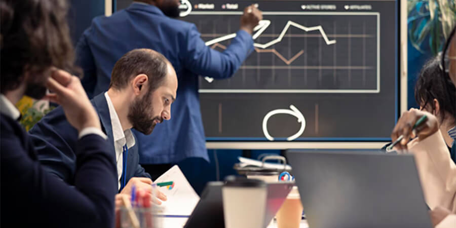 A group of colleagues in a business meeting, analysing a line graph on a large digital screen.