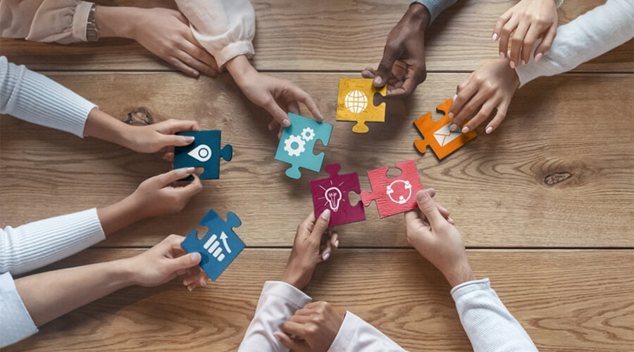 Overhead view of a team's hands assembling colorful jigsaw pieces on a wooden table, symbolizing collaboration and problem-solving.