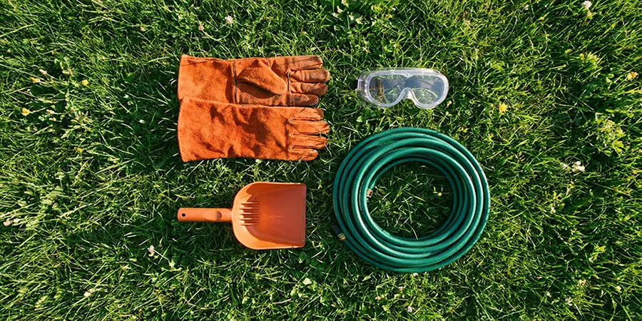 Essential gutter cleaning tools including gloves, goggles, and a scoop arranged on a lawn