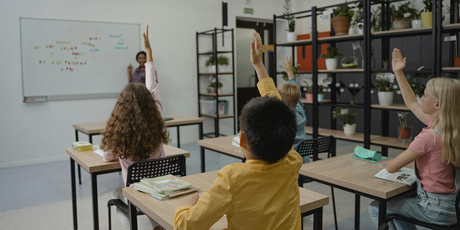 Children in a classroom with their hands up to answer a question.