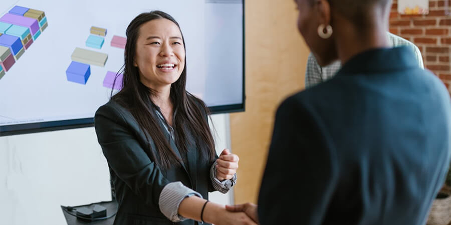 Two professional women shake hands in an office.