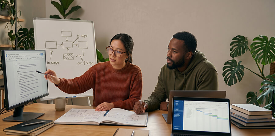 Two people discuss project data on a monitor and laptop, with a 'scope' flowchart in the background.