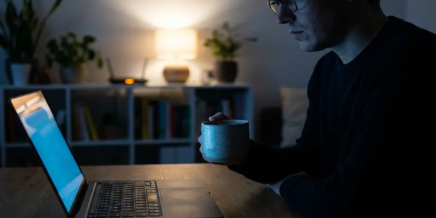 Person relaxing in a dimly lit room illuminated by a laptop screen, representing online privacy