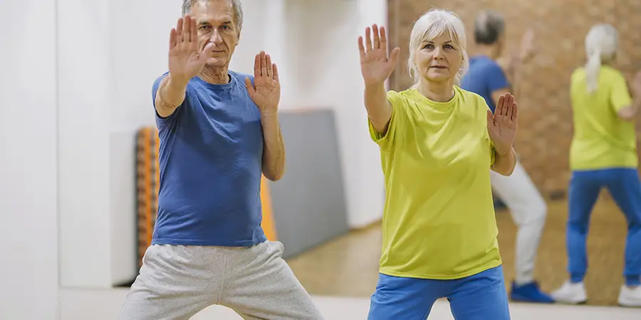 A retired couple performing coordinated Tai Chi movements together in a studio