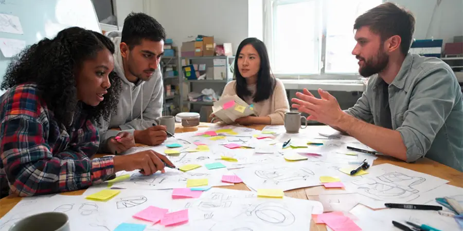 Group of people sitting around a table with many sheets of paper and sticky notes.