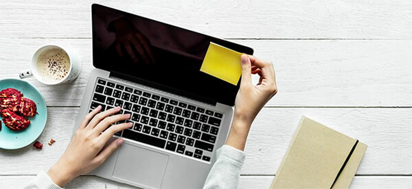 Woman's hands placing a post-it note on a laptop screen.