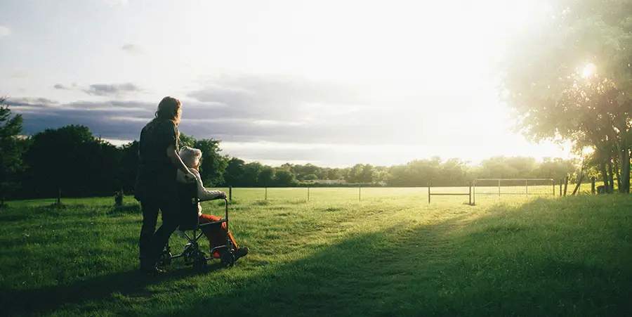 Eldely person being pushed across a field in a wheelchair during sunrise.