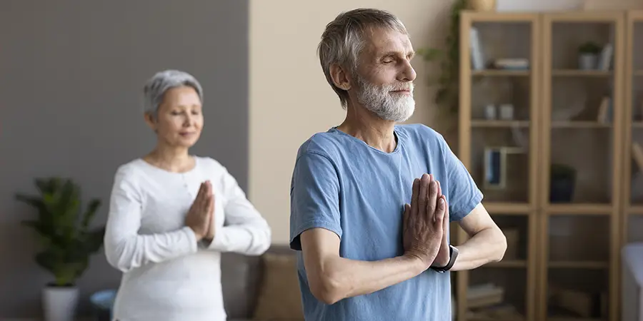 A senior man and woman practicing mindful breathing and meditation exercises indoors