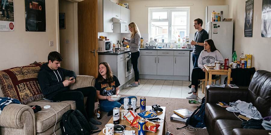 A group of students in a cluttered shared living and kitchen space.