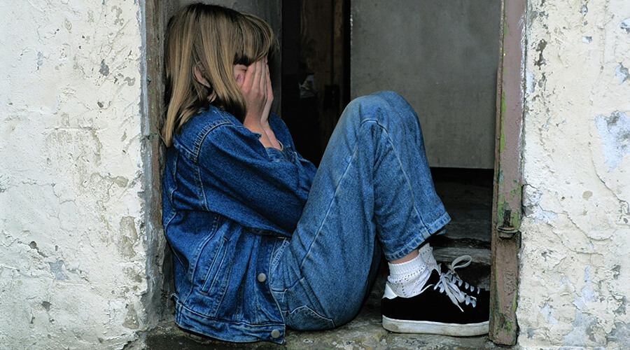 Girl child with her head in her hands sitting in a doorway.
