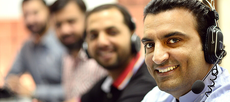 Close up of man with headset, blurred colleagues in the background.