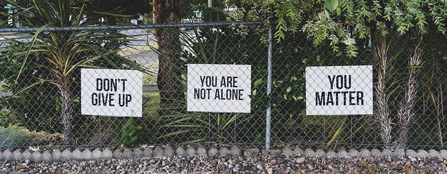 Three posters behind a fence reading, 'Don't Give Up', 'You are Not Alone' and 'You Matter'.